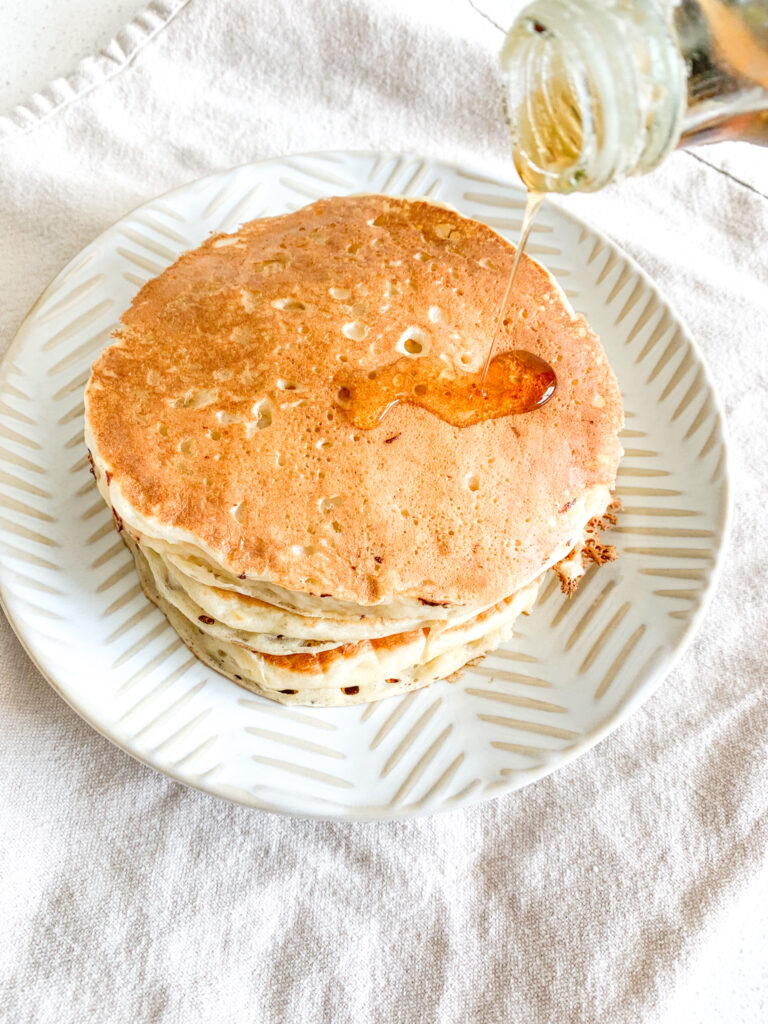maple syrup getting poured over a stack of sourdough discard buttermilk pancakes