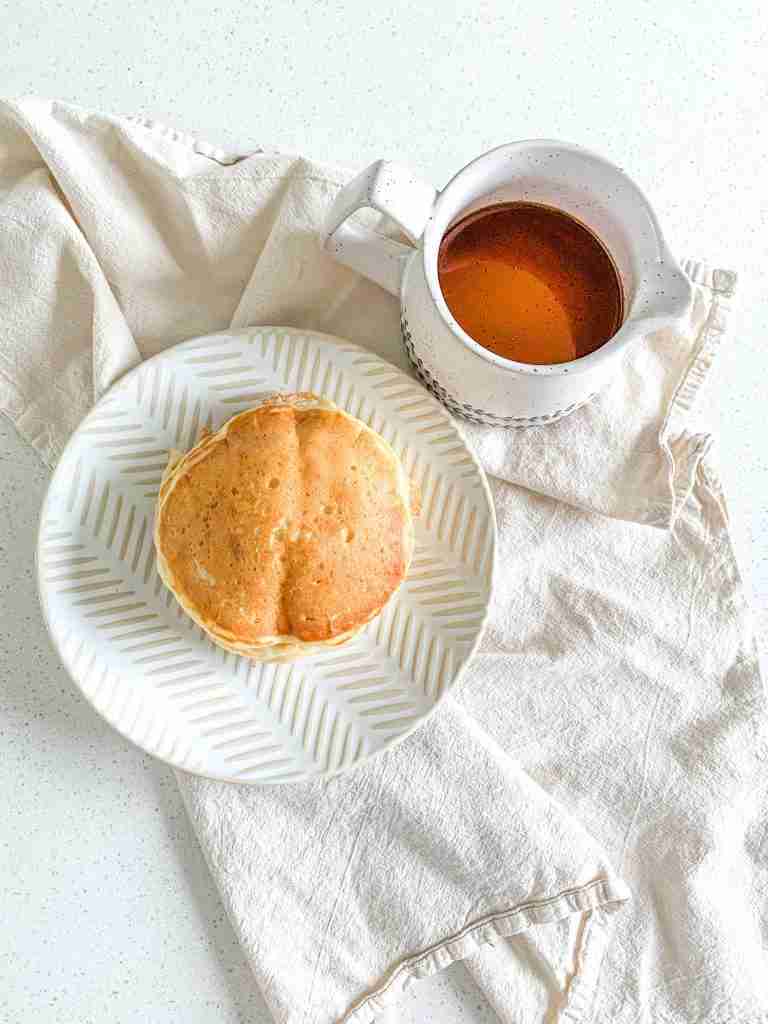 a freshly made stack of sourdough buttermilk pancakes with a container of syrup beside them