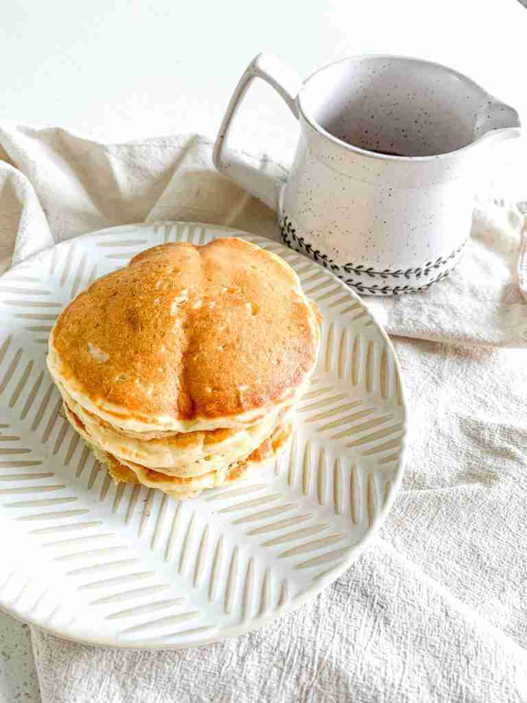 a freshly made stack of sourdough buttermilk pancakes with a container of syrup beside them