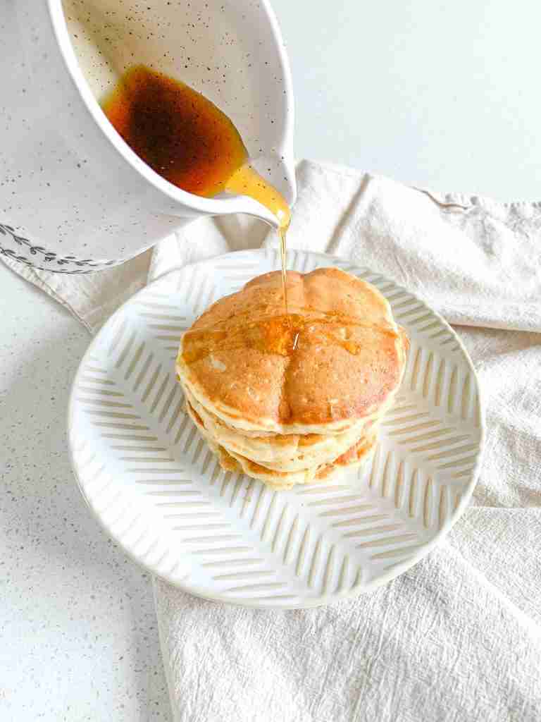 maple syrup getting poured over a freshly made stack of sourdough buttermilk pancakes