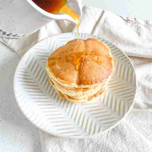 maple syrup getting poured over a freshly made stack of sourdough buttermilk pancakes