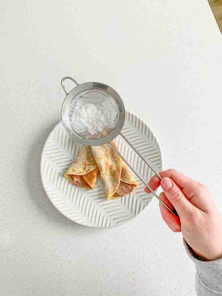dusting filled sourdough crepes with powdered sugar