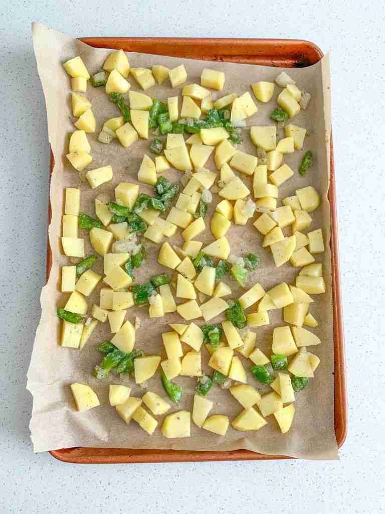 potatoes and peppers on a sheet pan ready to be baked for bacon breakfast burritos