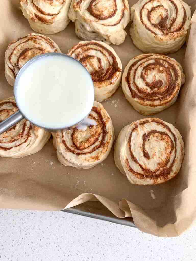 milk being poured over shaped sourdough maple cinnamon rolls before baking