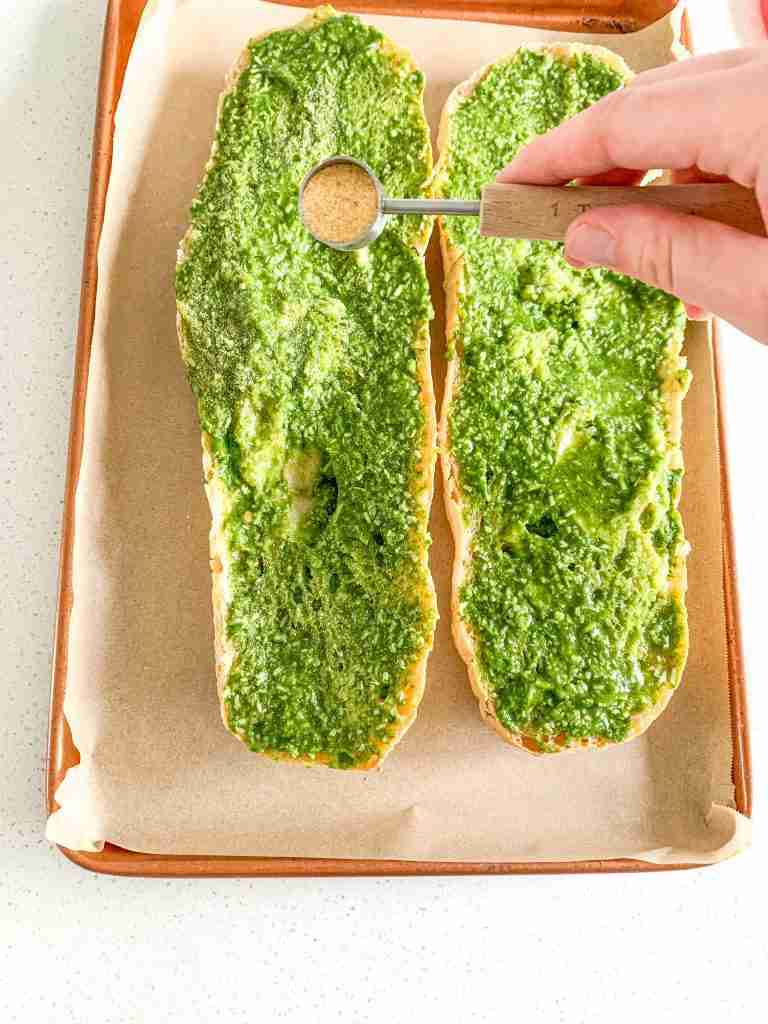 garlic powder being sprinkled on pesto French bread for sourdough pesto garlic bread