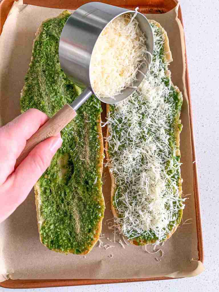 parmesan being sprinkled on pesto French bread for sourdough pesto garlic bread