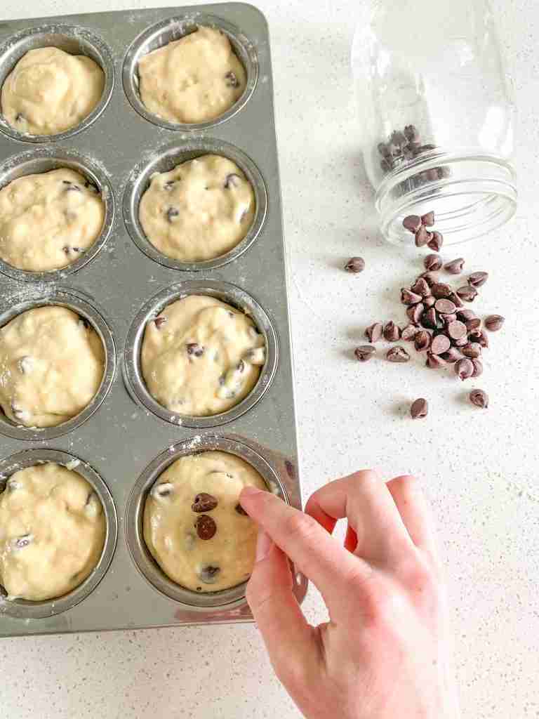 sourdough chocolate chip muffins dough scooped into a muffin pan getting topped with chocolate chips