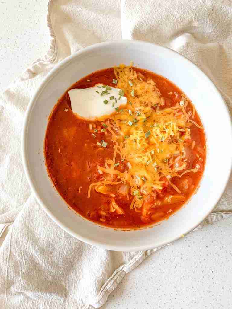 freshly cooked mexican chicken and rice soup in a bowl topped with cheese, sour cream, and chives