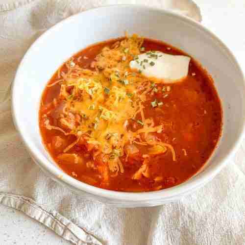 freshly cooked mexican chicken and rice soup in a bowl topped with cheese, sour cream, and chives