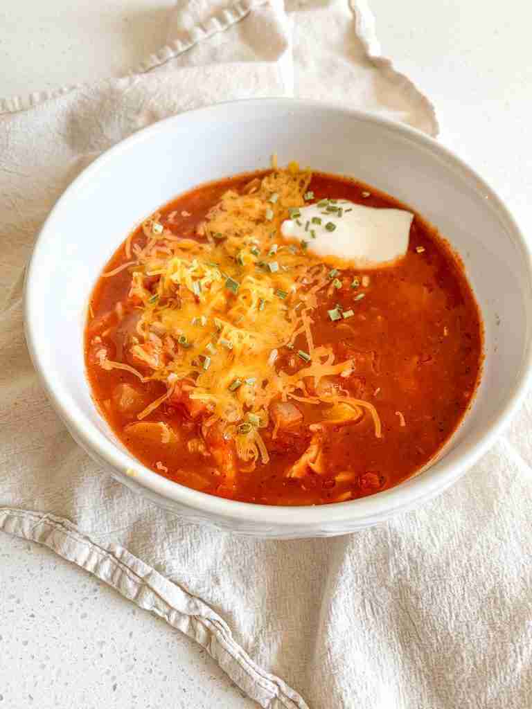 freshly cooked mexican chicken and rice soup in a bowl topped with cheese, sour cream, and chives