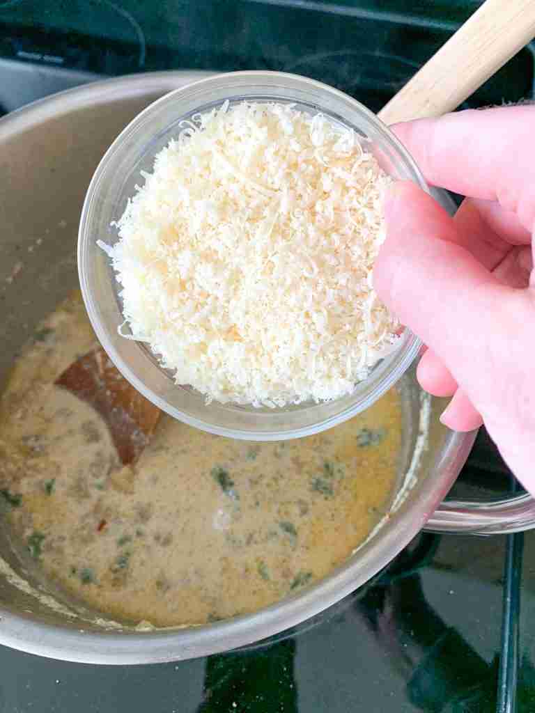 grated parmesan being added to pot for Creamy Parmesan Italian Sausage Soup