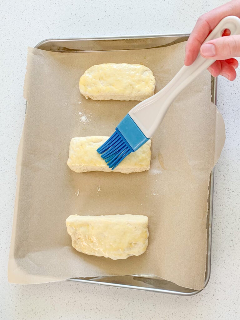 brushing sliced biscuits with melted butter before bakinig