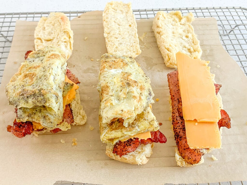 layering eggs, cheese, and bacon on biscuits