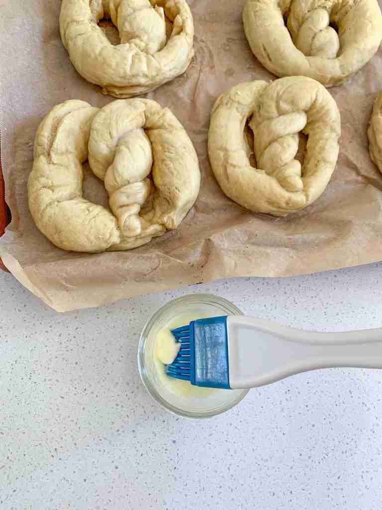 boiled soft sourdough pretzels getting brushed with butter before baking