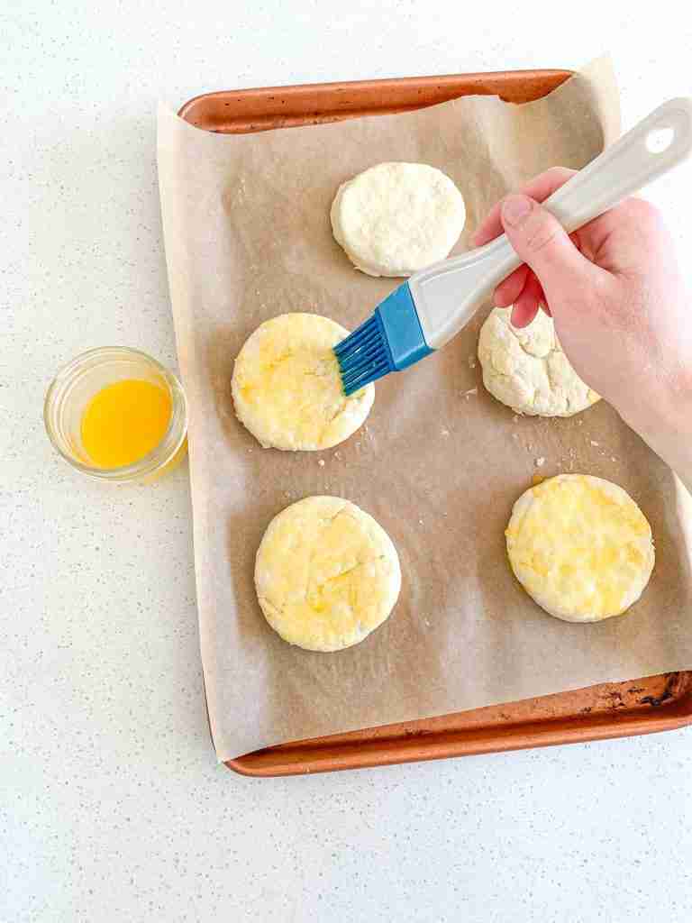 brushing biscuits with butter before they go in the oven for sourdough breakfast sandwiches