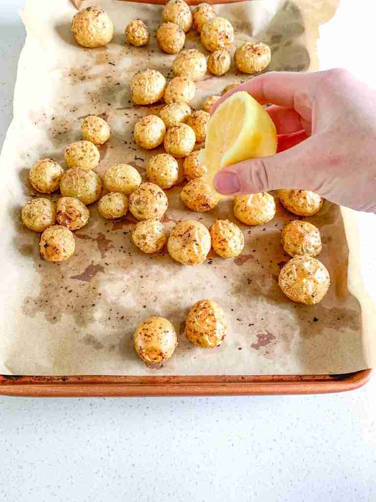 freshly roasted lemon potatoes getting lemon juice squeezed over them