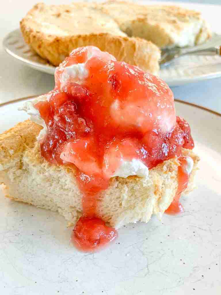 freshly baked sourdough angel food cake with a slice topped with strawberries and whipped cream