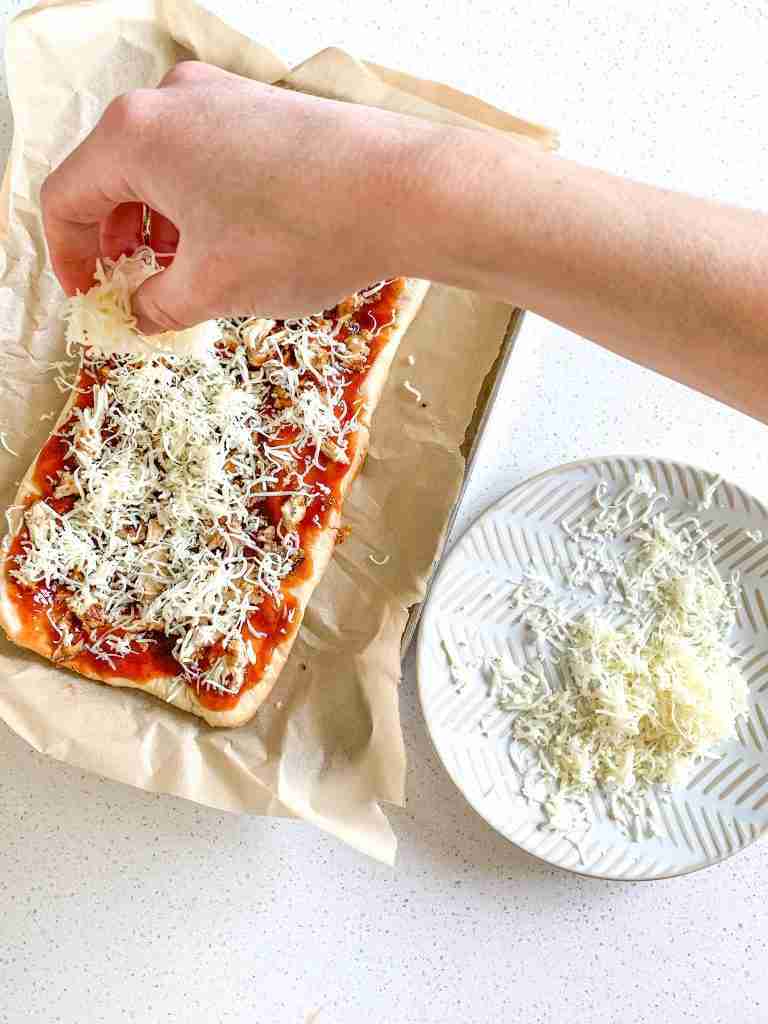 adding cheese to a flatbread pizza