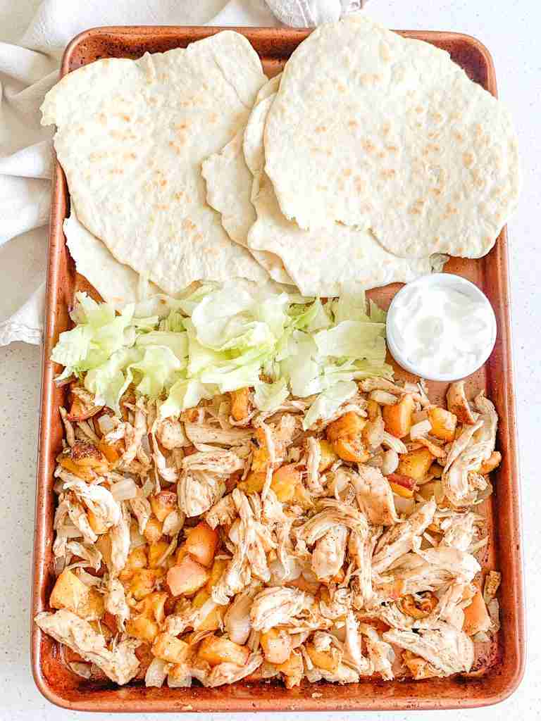 freshly cooked chipotle chicken peach tacos on a sheet pan with tortillas and fixings