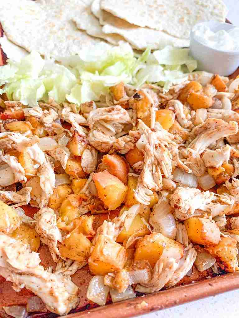 freshly cooked chipotle chicken peach tacos on a sheet pan with tortillas and fixings