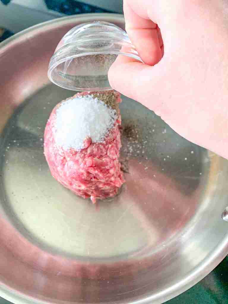 adding seasonings to beef in a skillet