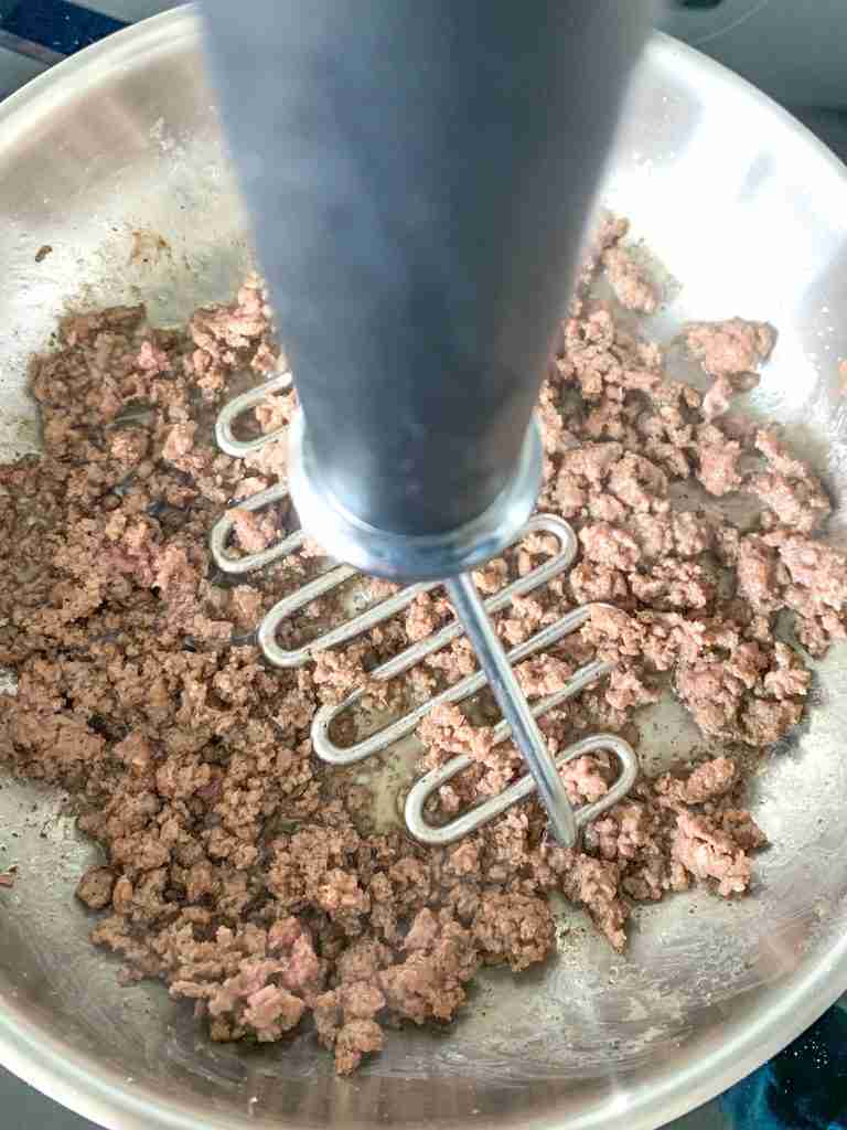 using a masher to break up ground beef while cooking