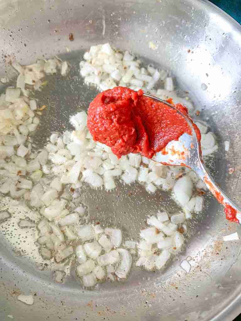 adding tomato paste to a skillet with onion