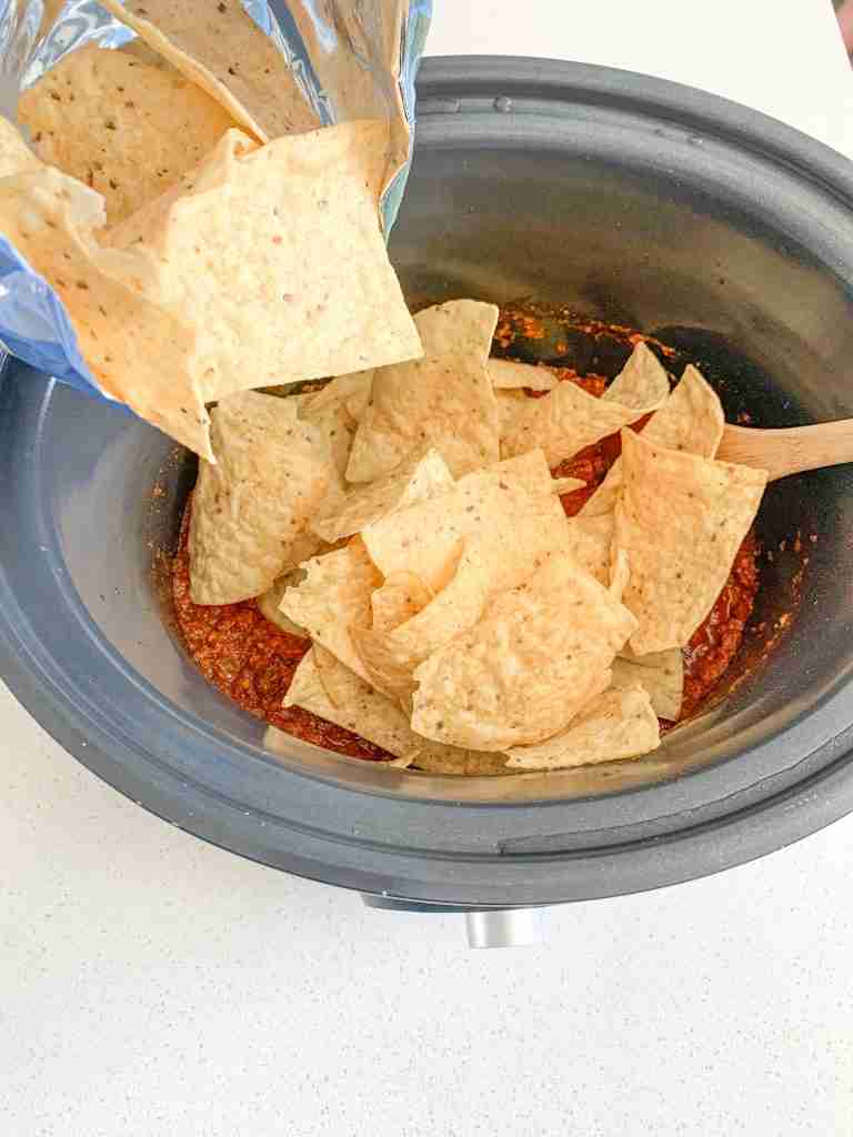 adding tortilla chips to cooked walking taco meat in slow cooker