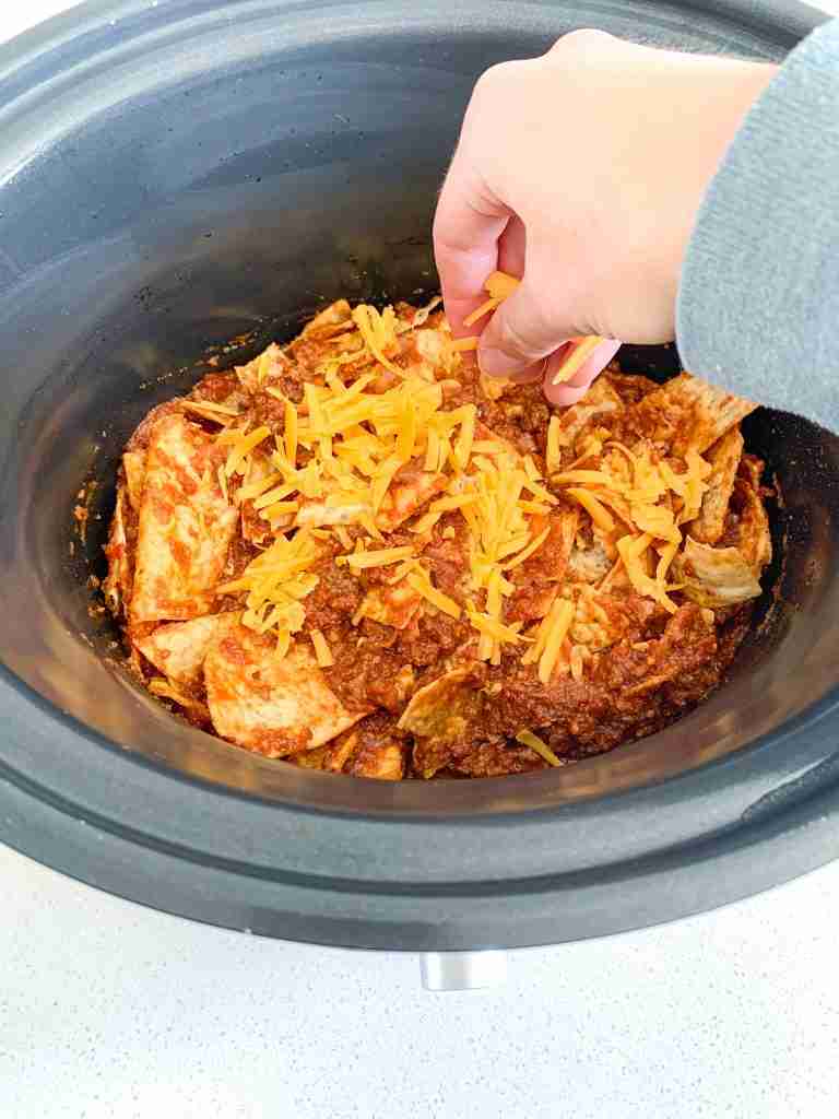 adding cheese to walking taco casserole in slow cooker