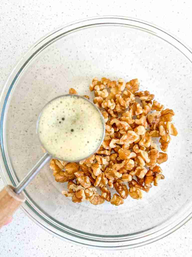 adding brown butter to walnuts in a bowl