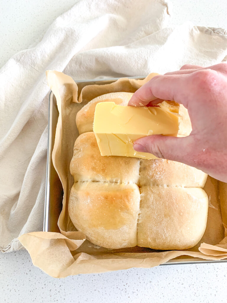 spreading butter on top of baked hawaiian rolls