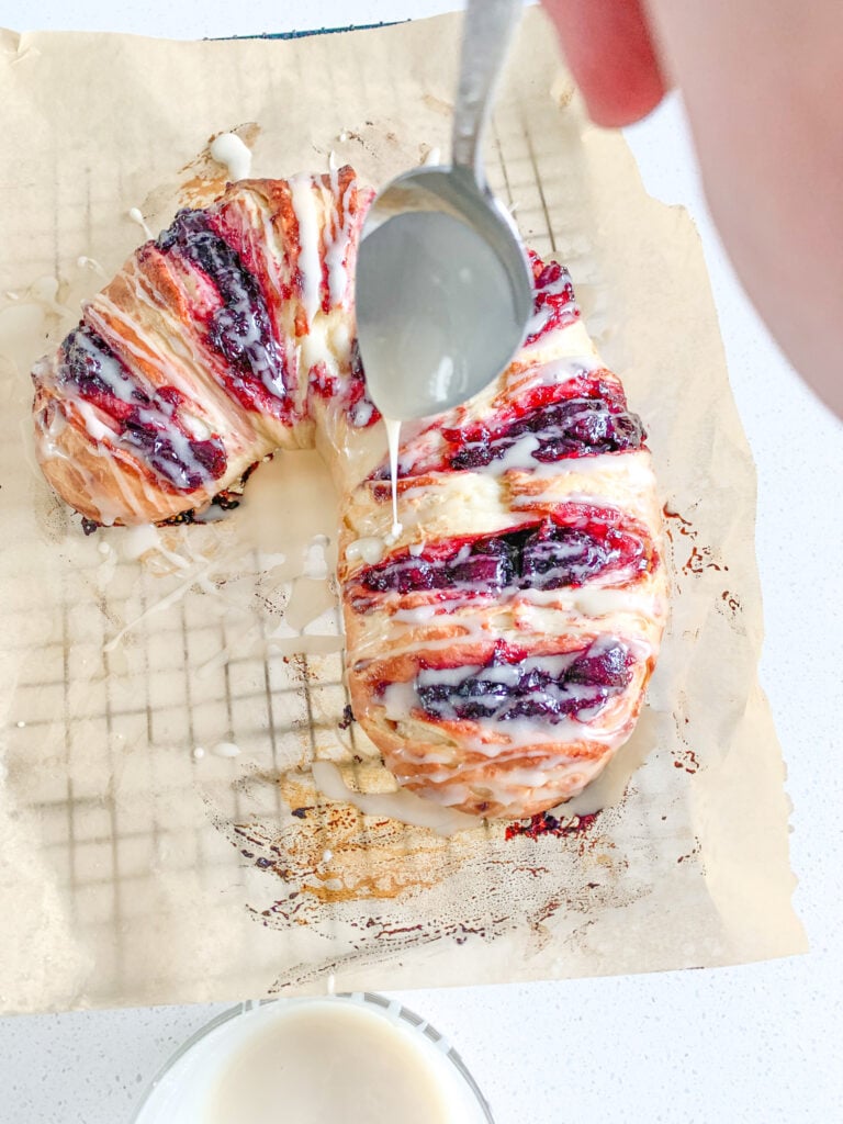 adding glaze to freshly baked sourdough candy cane danish