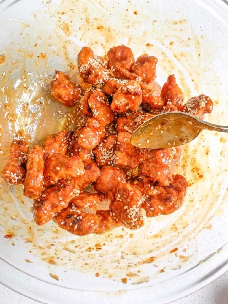 tossing chicken with general tso's sauce and sesame seeds