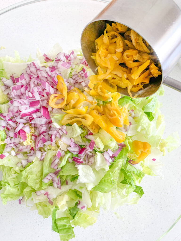 adding sliced and drained pepperoncini peppers to salad bowl