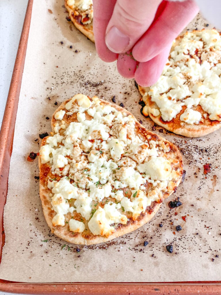freshly baked feta naan pizza getting sprinkled with dried parsley