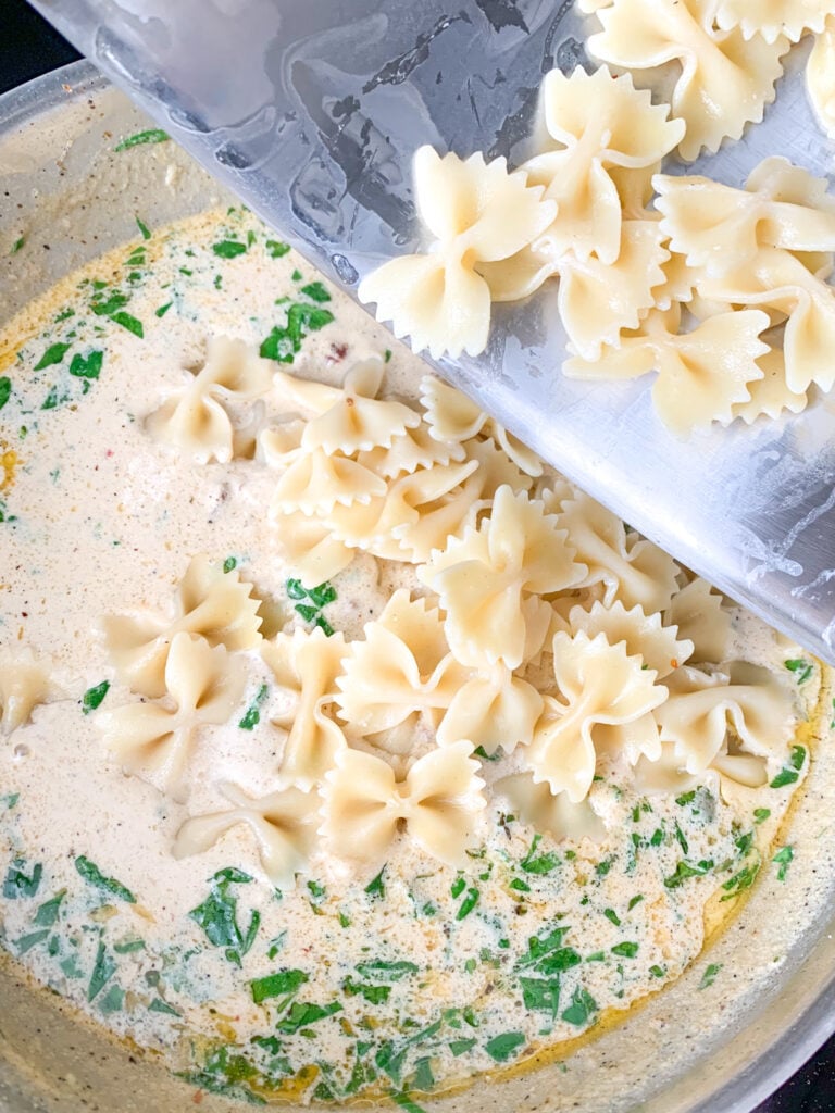adding cooked pasta to tuscan pasta sauce