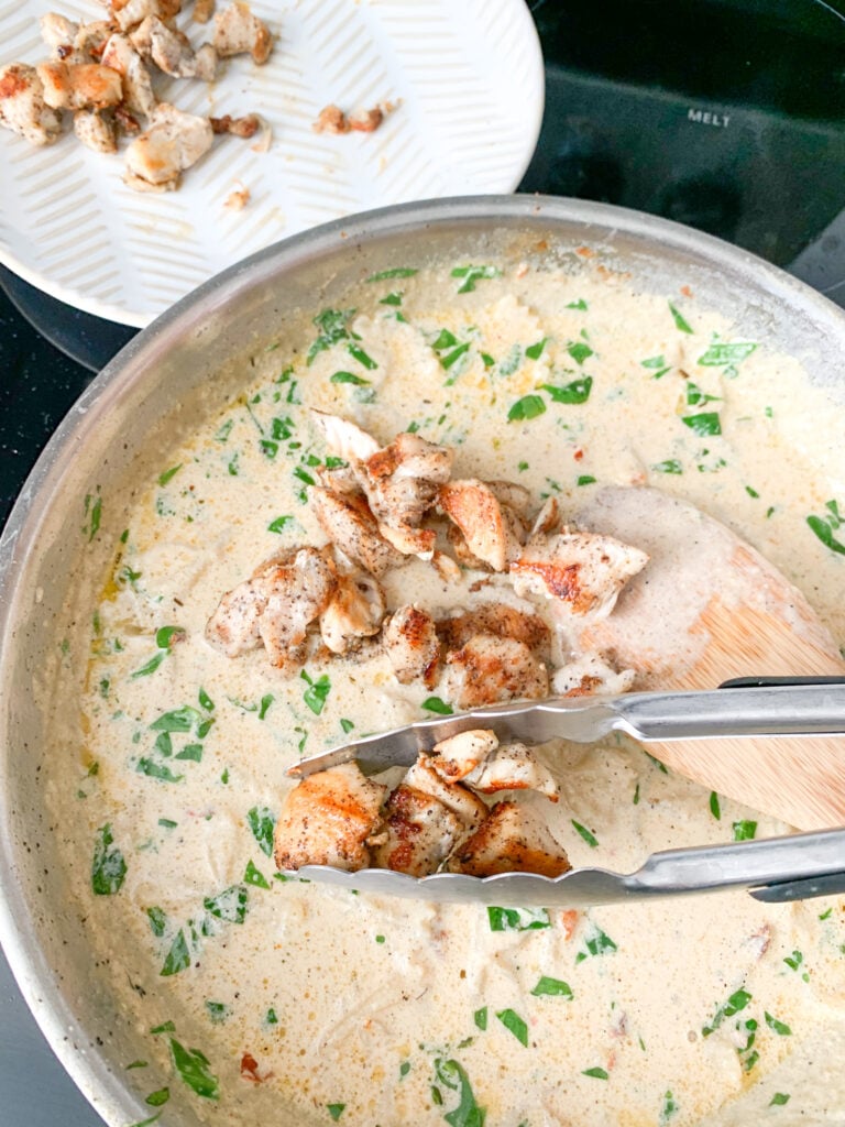 adding chicken to tuscan pasta sauce