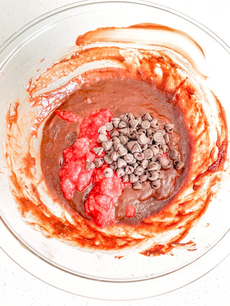 adding chocolate chips and raspberries to brownie batter