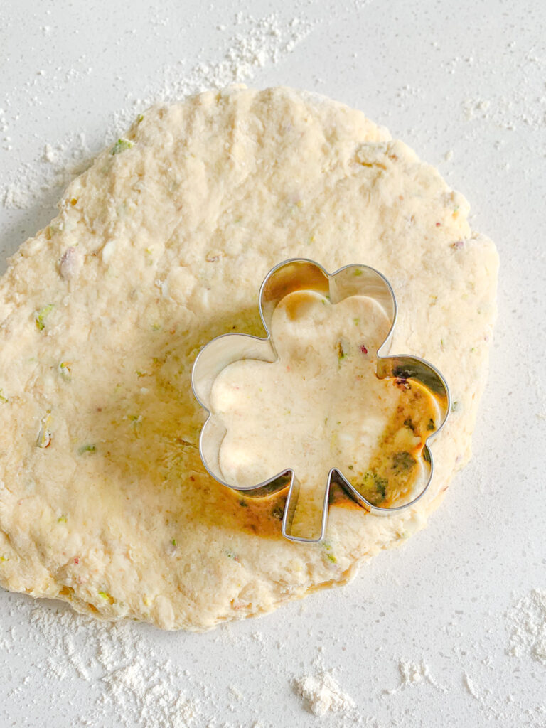 cutting sourdough scone dough out with a shamrock cookie cutter