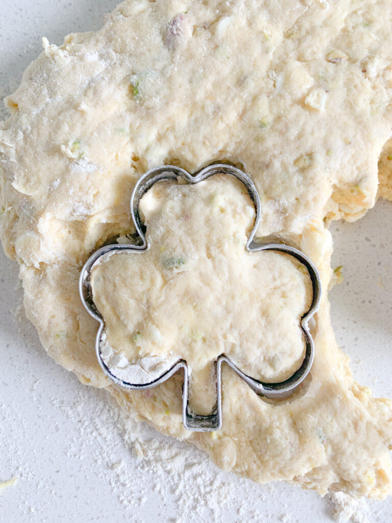 cutting sourdough scone dough out with a shamrock cookie cutter