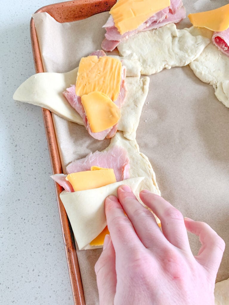 rolling up ham and cheese into crescent rolls for ring