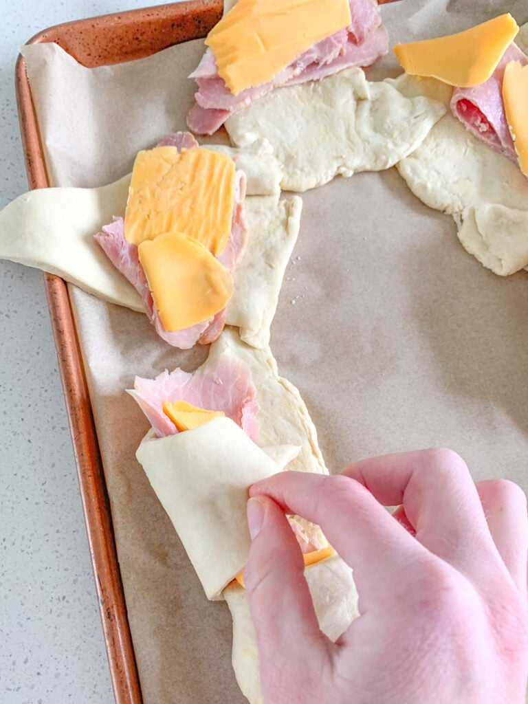rolling up ham and cheese into crescent rolls for ring