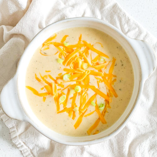 freshly cooked cheesy potato soup in a bowl with shredded cheese and green onions on top
