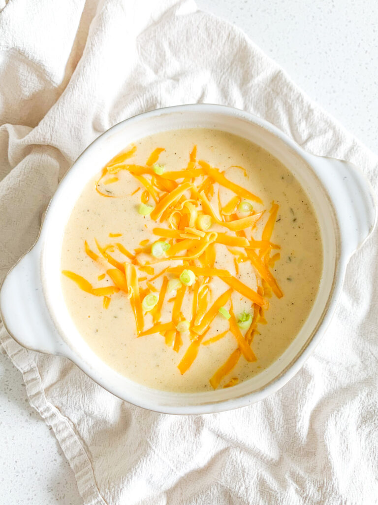 freshly cooked cheesy potato soup in a bowl with shredded cheese and green onions on top