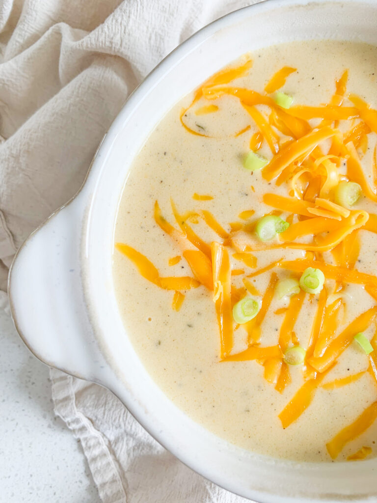 freshly cooked cheesy potato soup in a bowl with shredded cheese and green onions on top
