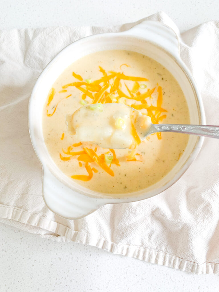 freshly cooked cheesy potato soup in a bowl with shredded cheese and green onions on top