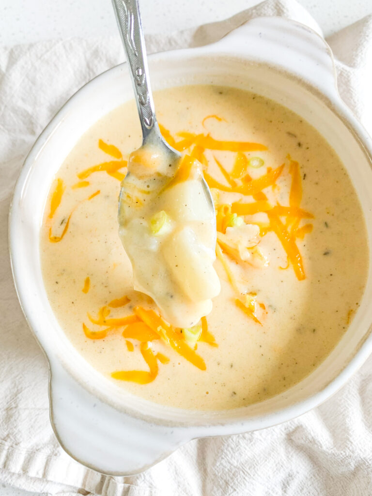freshly cooked cheesy potato soup in a bowl with shredded cheese and green onions on top