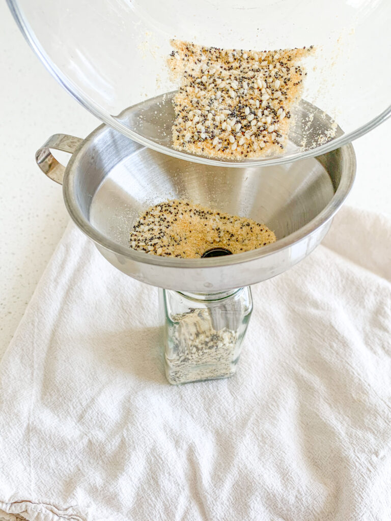 pouring everything bagel seasoning into an old spice jar for storage