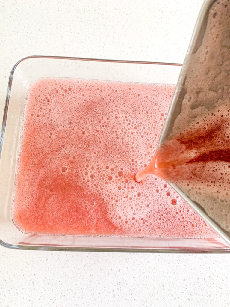 pouring strawberry jello mixture into a storage dish for cooling