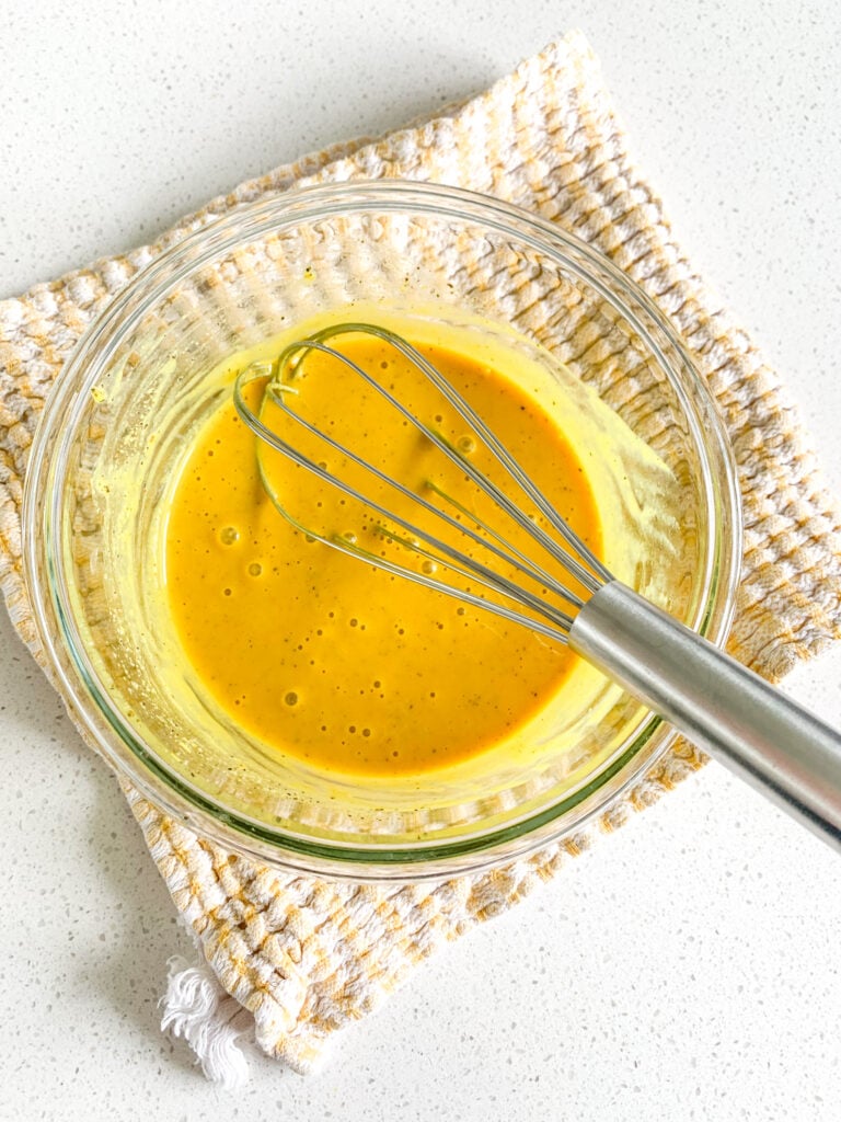 mixing together gold bbq sauce ingredients with a whisk in a bowl